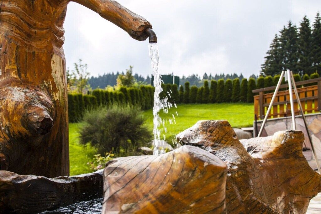 A wooden water feature with a flowing stream, surrounded by a well-maintained garden and a wooden deck.