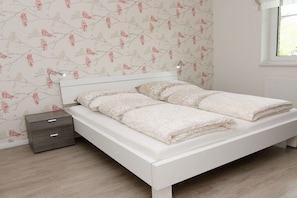 Ein Schlafzimmer mit einem weißen Bett, einem Nachttisch und einer Wand mit Blumenmuster.