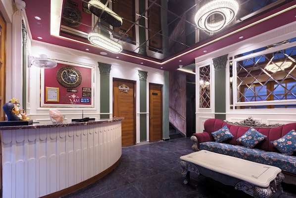 A hotel lobby with a reception desk, a sofa set, and a chandelier.