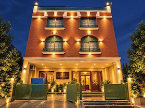 A hotel with a brick facade, multiple windows with green frames, and a welcoming entrance with steps and potted plants.
