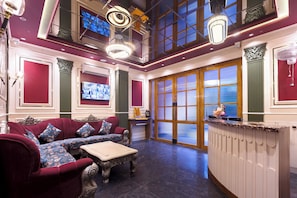 A hotel lobby with a red sofa set, a reception desk, and a large window with a view.