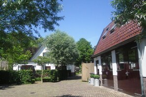 Een binnenplaats met een geplaveid pad, een gebouw met een rode dakbedekking en een houten omheining.
