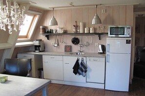 Een kleine keuken met een magnetron, koelkast en verschillende keukengerei dat aan de muur hangt.