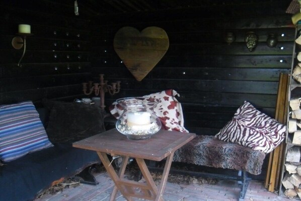 Interior rústico de uma cabana com um banco de madeira, uma mesa com uma vela e uma decoração em formato de coração na parede.