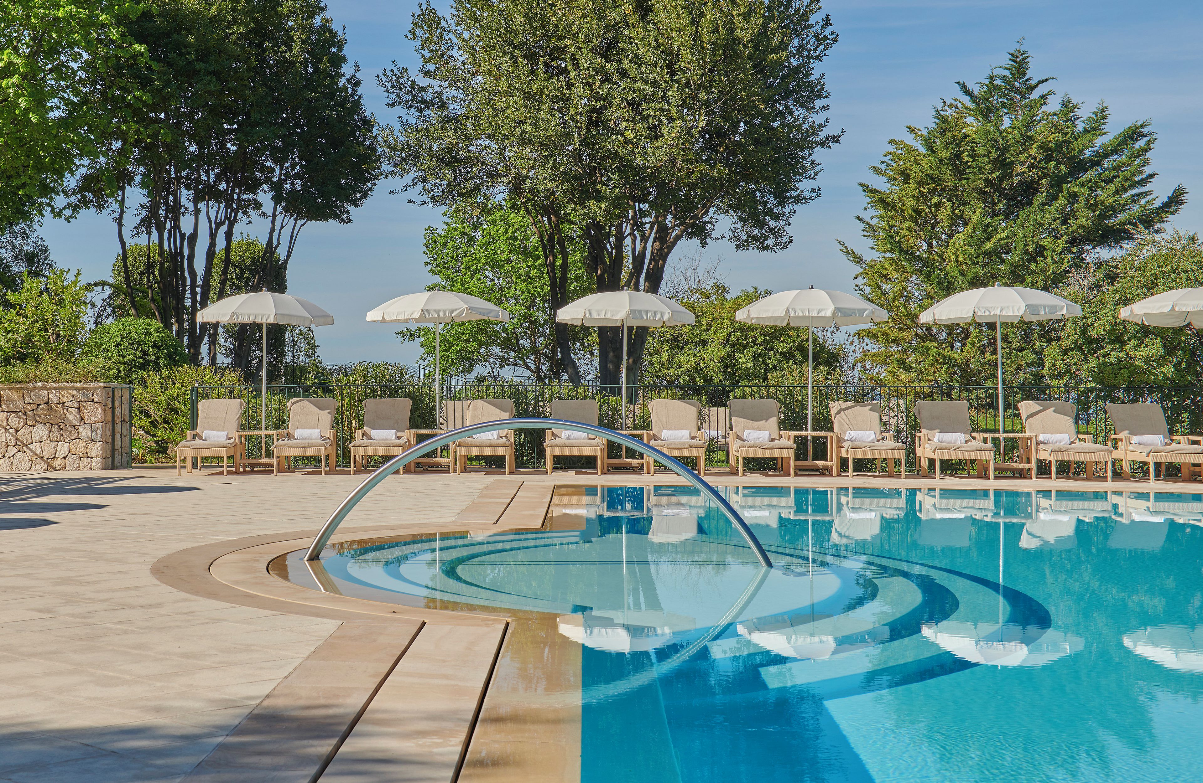 Un espace piscine agrémenté de chaises longues et de parasols, le tout entouré d’arbres.