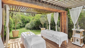 A wooden deck with two massage tables covered in white sheets, a wooden pergola overhead, and a white table with a 'bambord' sign. - Chateau Saint-martin & Spa (Vence)