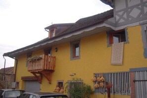 A yellow building with a balcony, a garage door, and a window with hanging bananas. - Holiday apartment with 1 bedroom (ANDLAU)
