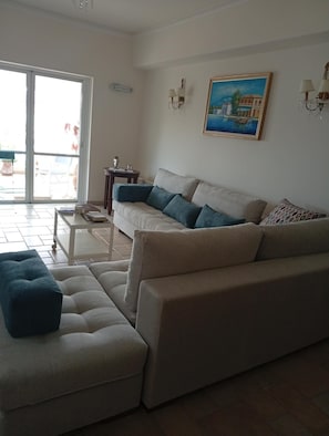 A living room with a sofa, ottoman, and a painting on the wall. - Elounda Sea View Maisonette (Schisma Eloundas)