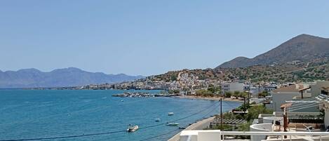 A coastal town with a clear view of the sea, boats, and a mountain in the distance.