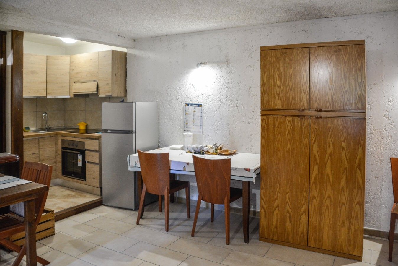 Eine kleine Küche mit Holzausstattung, einem Kühlschrank, einer Spüle und einem Esstisch mit Stühlen.