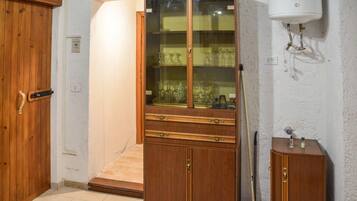 A room with a wooden wardrobe, a glass-fronted cabinet with wine glasses, a mop, and a water heater on the wall.