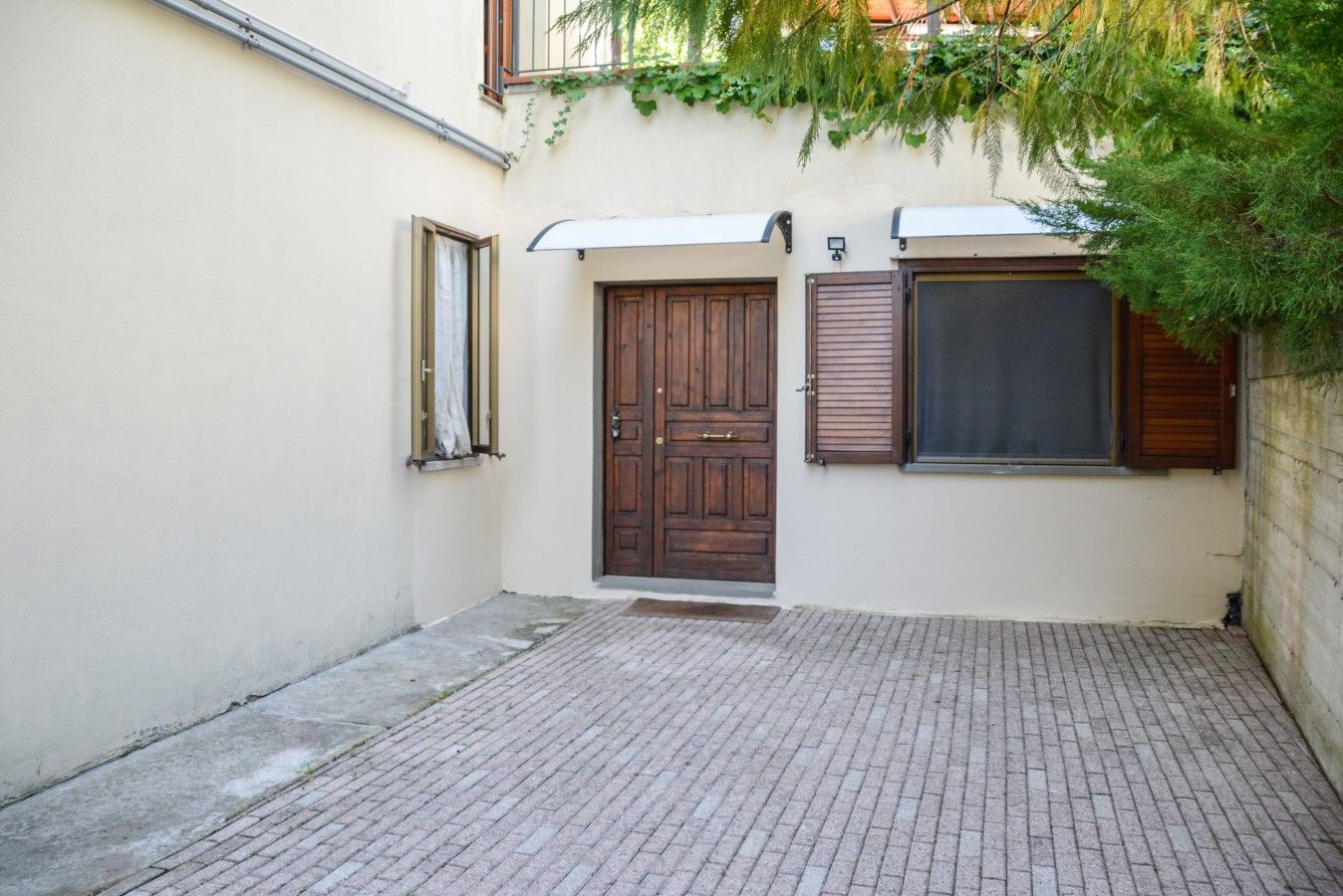 Un cortile con pavimento in pietra, una porta in legno e una finestra con persiane.