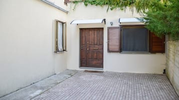 Un cortile con pavimento in pietra, una porta in legno e una finestra con persiane.