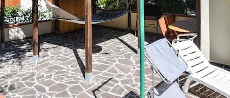 Eine Terrasse mit einer Hängematte, einem weißen Liegestuhl und einer Holzbank.