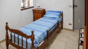 Ein Einzelbett mit Holzrahmen und einer blauen, gestreiften Bettdecke in einem Zimmer mit weißen Wänden und Fliesenboden.