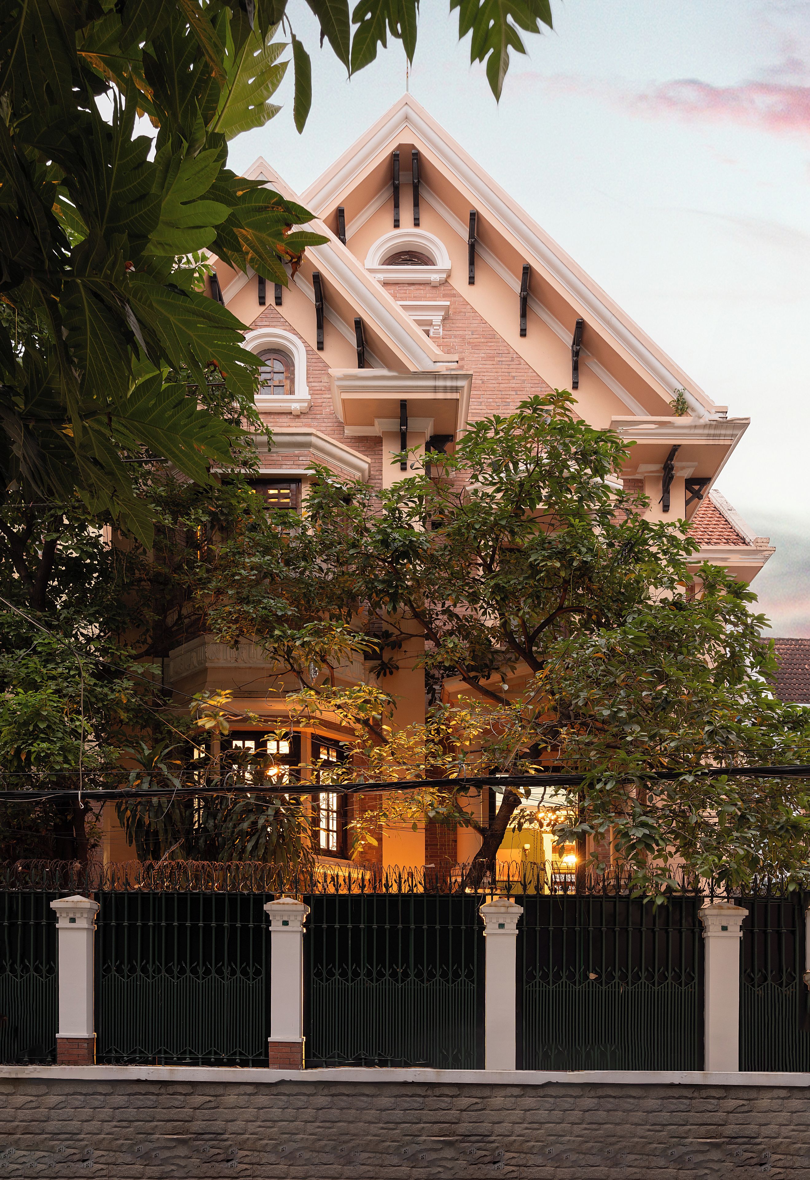 A large, multi-story building with a prominent central tower, surrounded by lush greenery and a black metal fence.