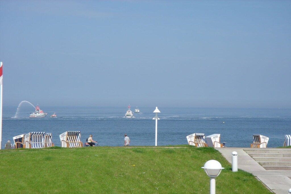 A coastal promenade with beach chairs, a lighthouse, and boats in the distance.