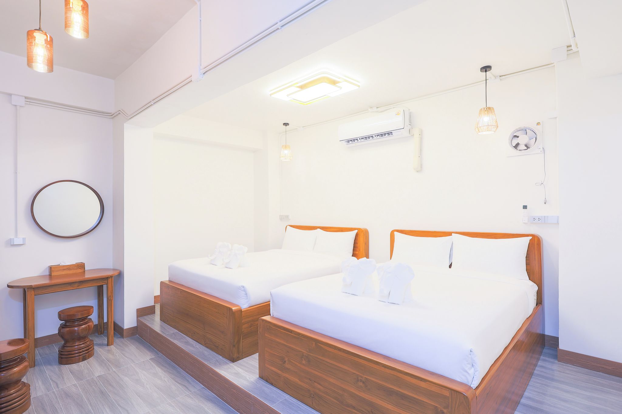 Ein Hotelzimmer mit zwei Betten, einem kleinen Tisch, einem Spiegel und einem Deckenventilator.