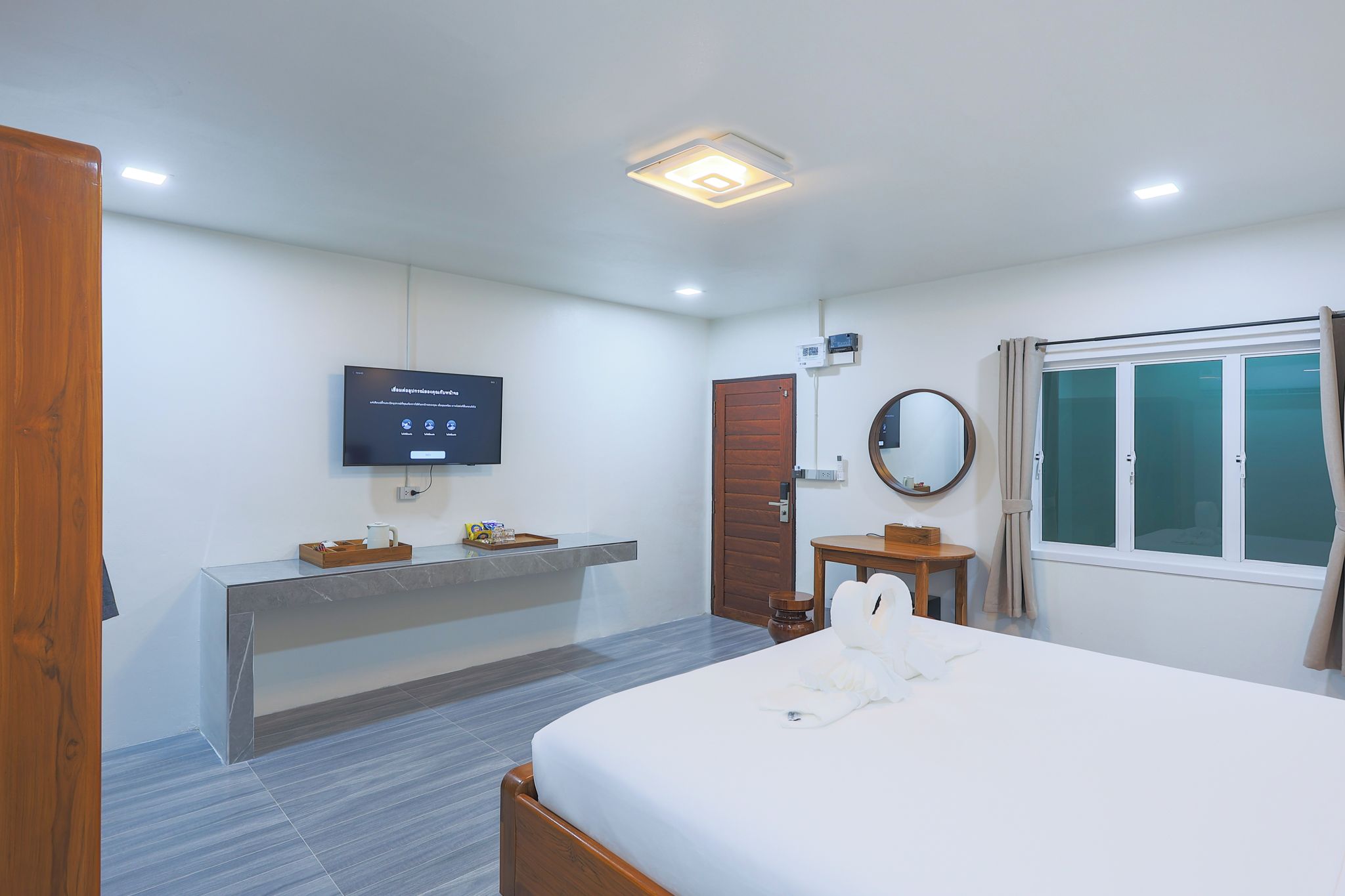 Ein Hotelzimmer mit Bett, Schreibtisch, Fernseher, Spiegel und einem Fenster mit Vorhängen.