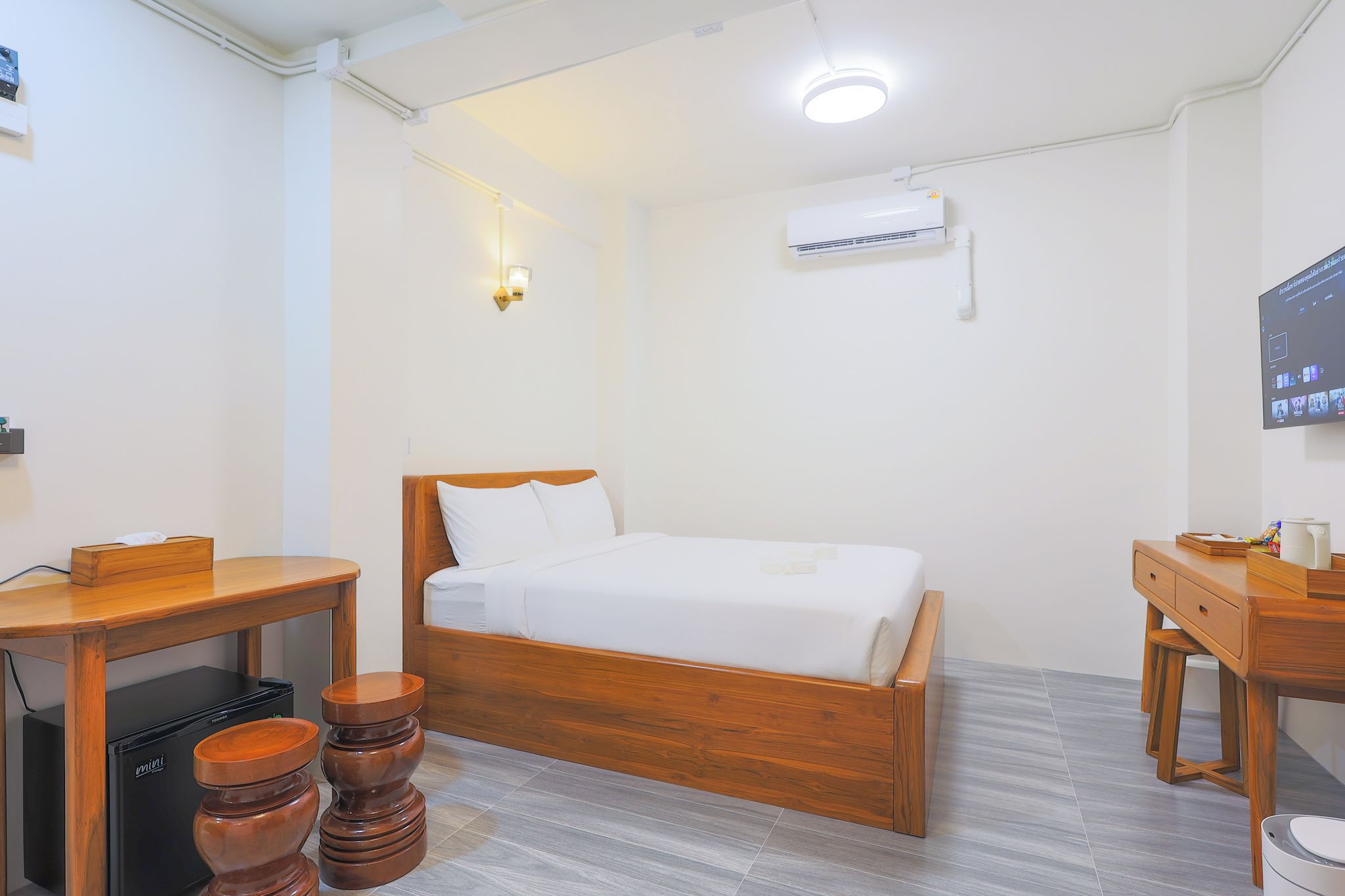 A hotel room with a wooden bed, a desk, a chair, a small table, and a television.