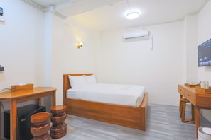 Quarto de hotel com cama de madeira, escrivaninha, cadeira, mesa pequena e televisão.