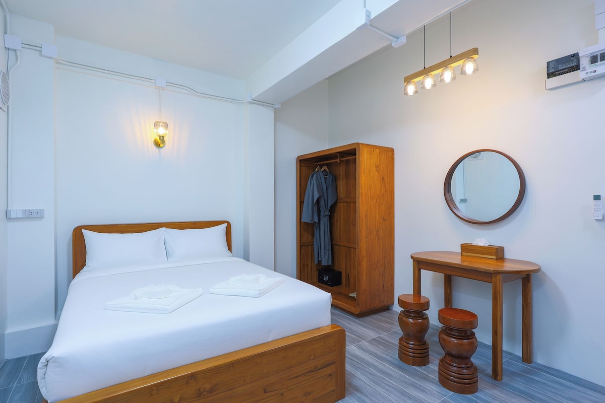 Una habitación de hotel con una cama de madera, un armario, un espejo redondo y una pequeña mesa de madera.