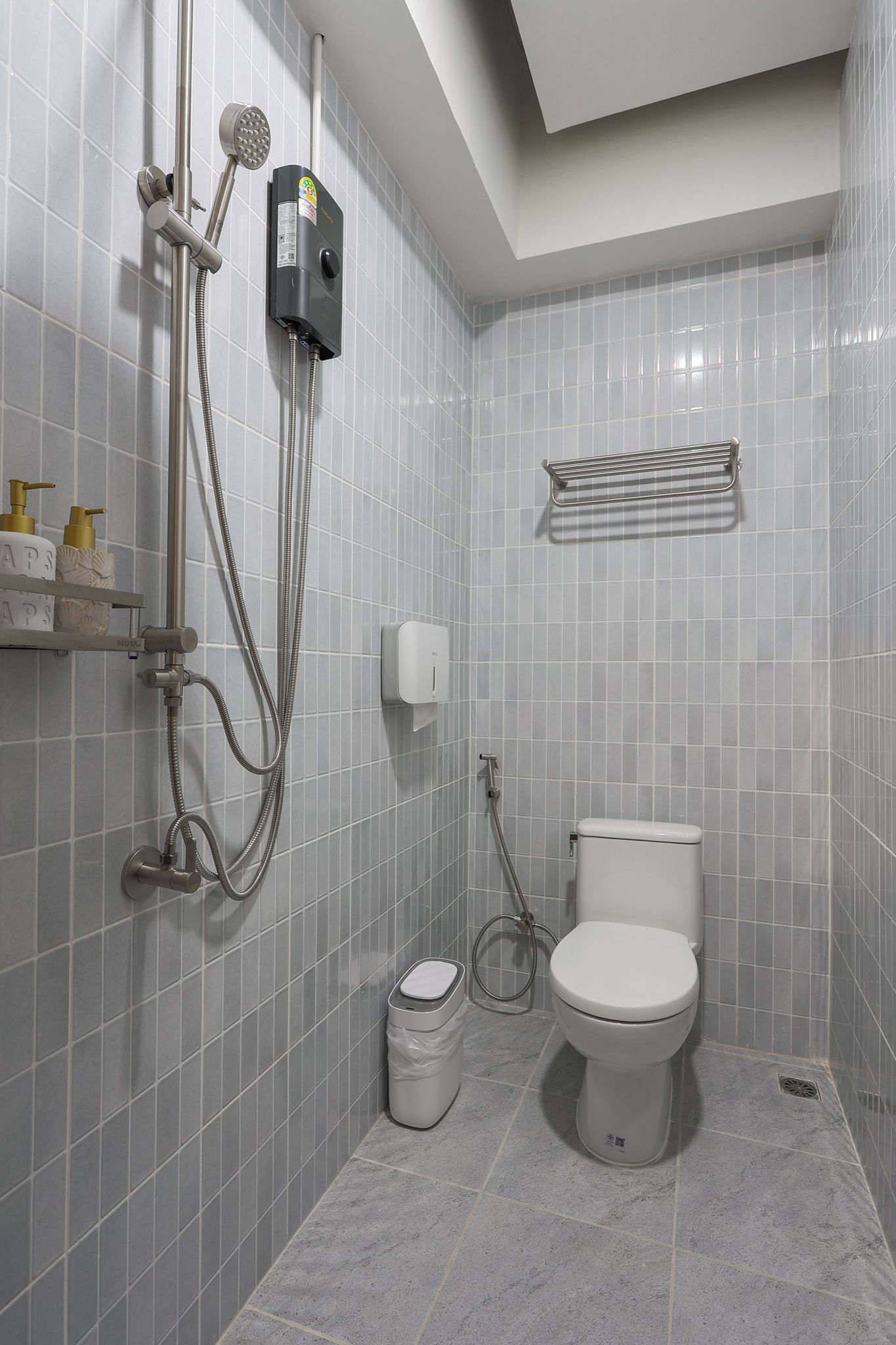 A bathroom with a toilet, a shower with a handheld showerhead, a towel rack, and a waste bin.