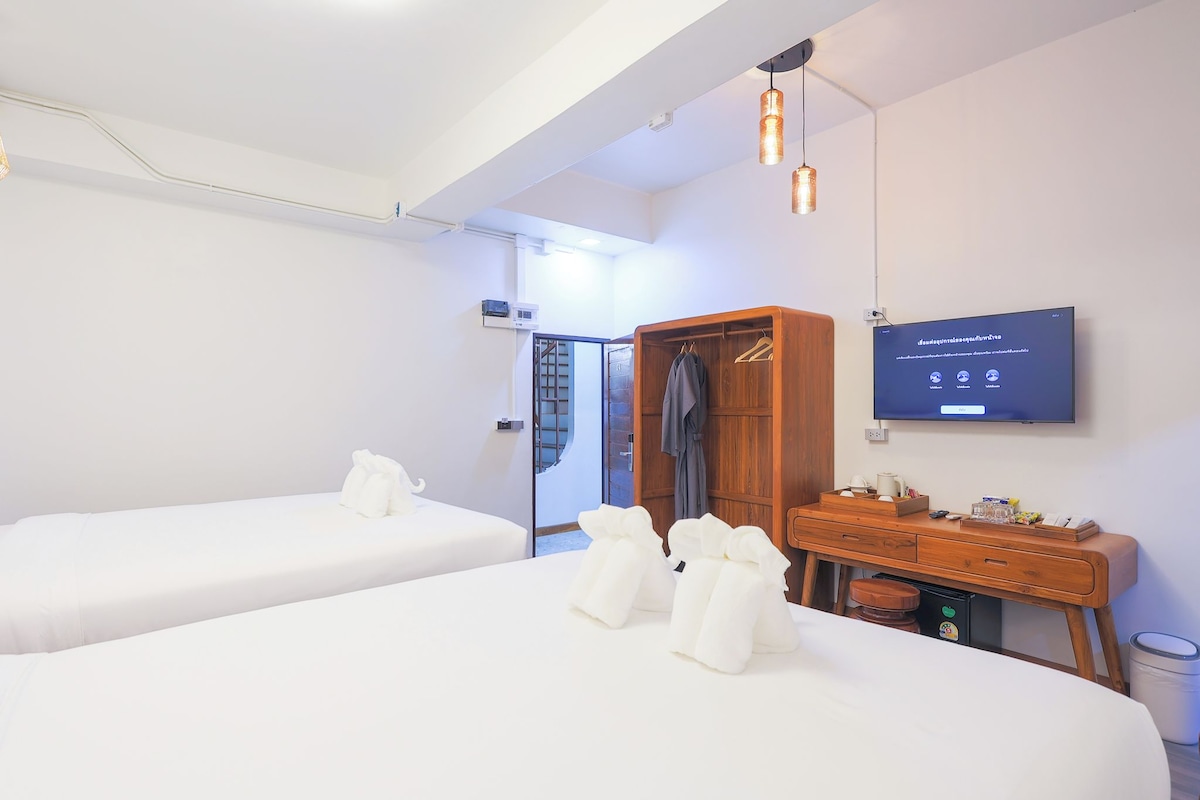 Een hotelkamer met twee bedden, een houten garderobe, een bureau met een televisie en een badkamers deur.