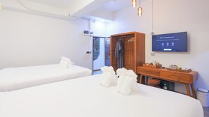 Habitación de hotel con dos camas, un armario de madera, un escritorio con televisor y la puerta del baño.