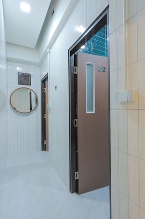 A hallway with white tiled walls, a wooden door with a number, and a round mirror. - Corner boutique hotel phuket (Phuket)
