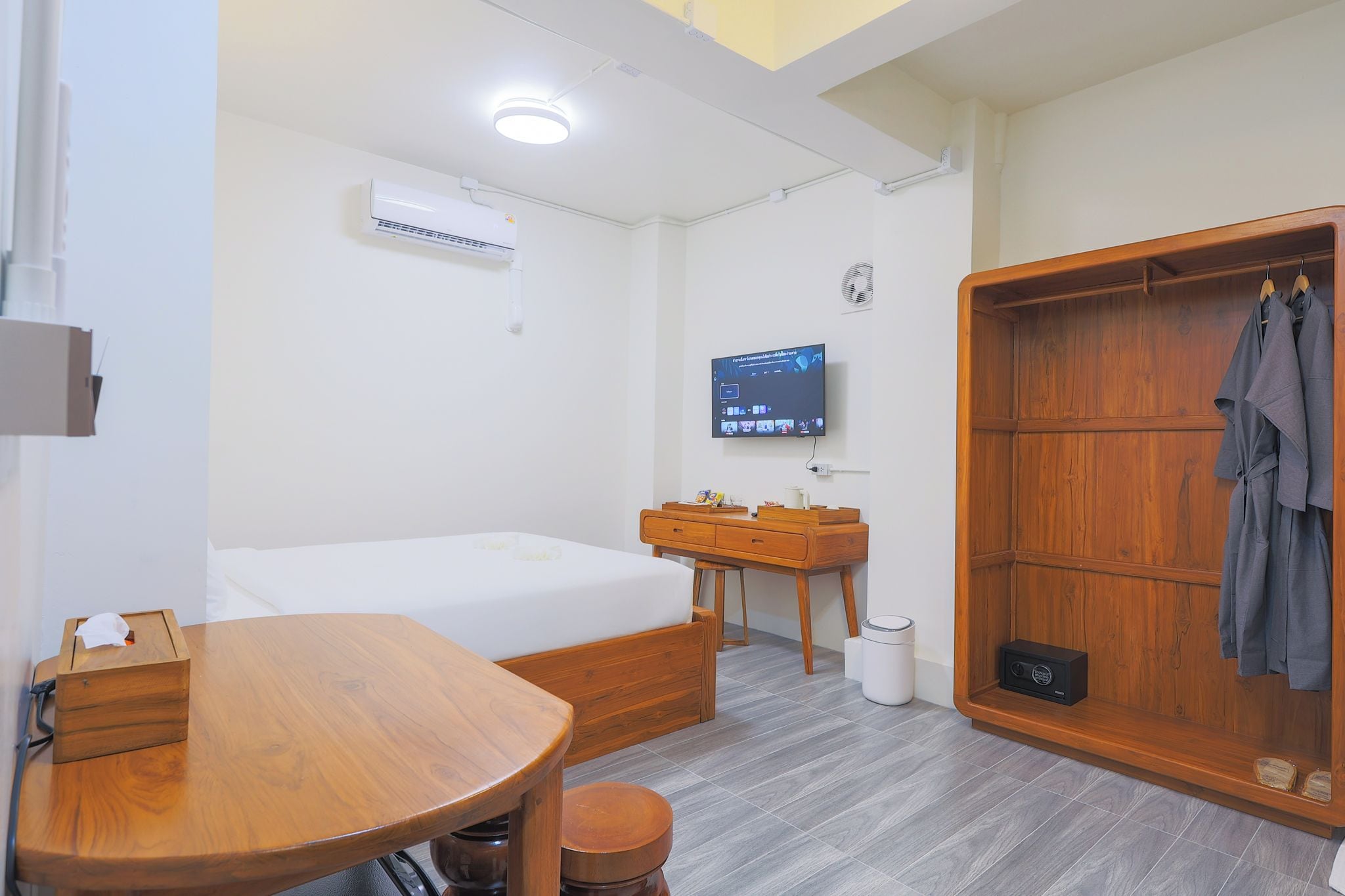 A hotel room with a bed, a desk, a wardrobe, a television, and a small trash bin.