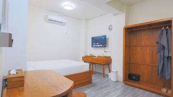 A hotel room with a bed, a desk, a wardrobe, a television, and a small trash bin.