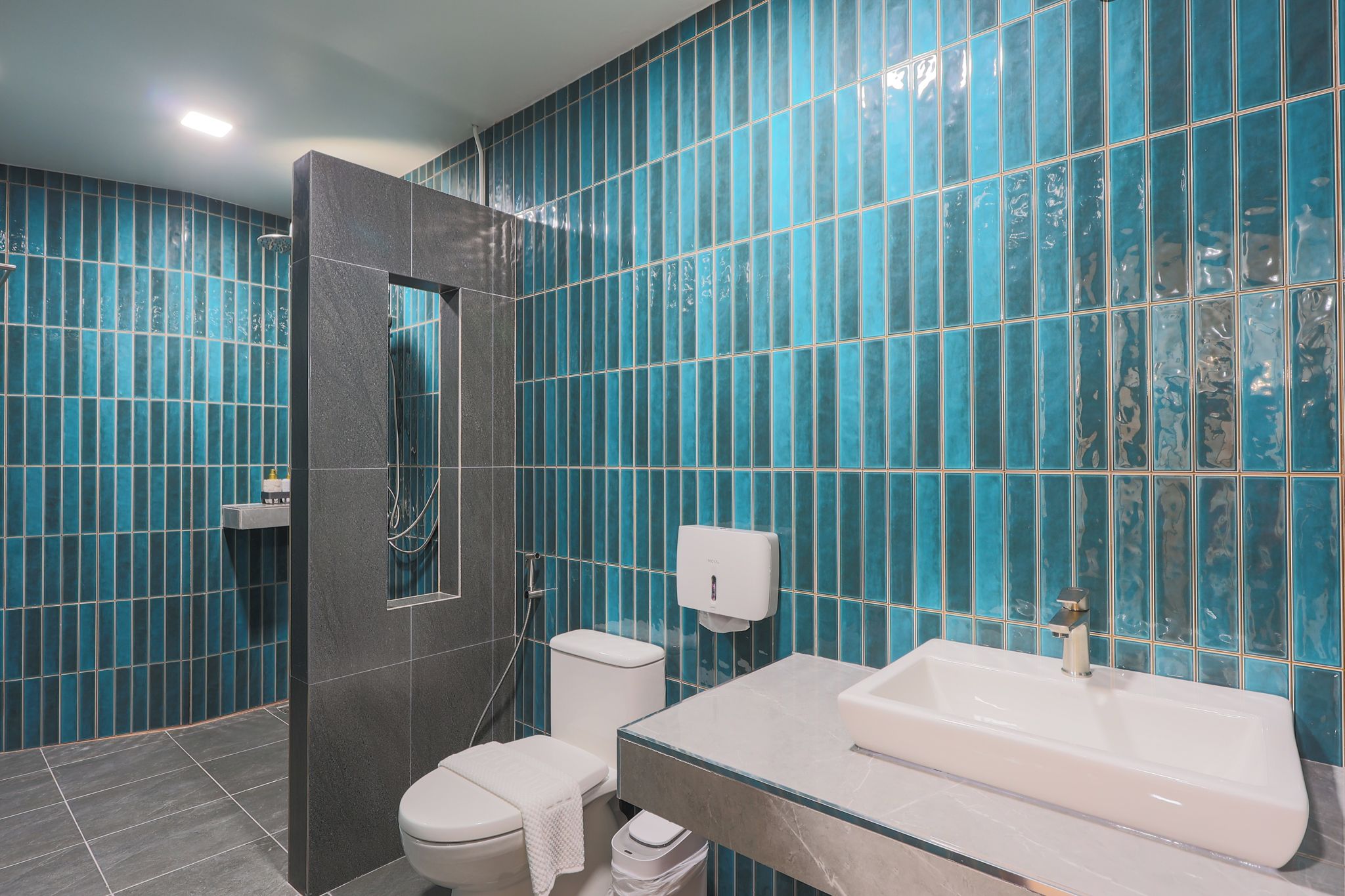 A modern bathroom with a glass shower enclosure, a toilet, a sink, and a hand dryer.