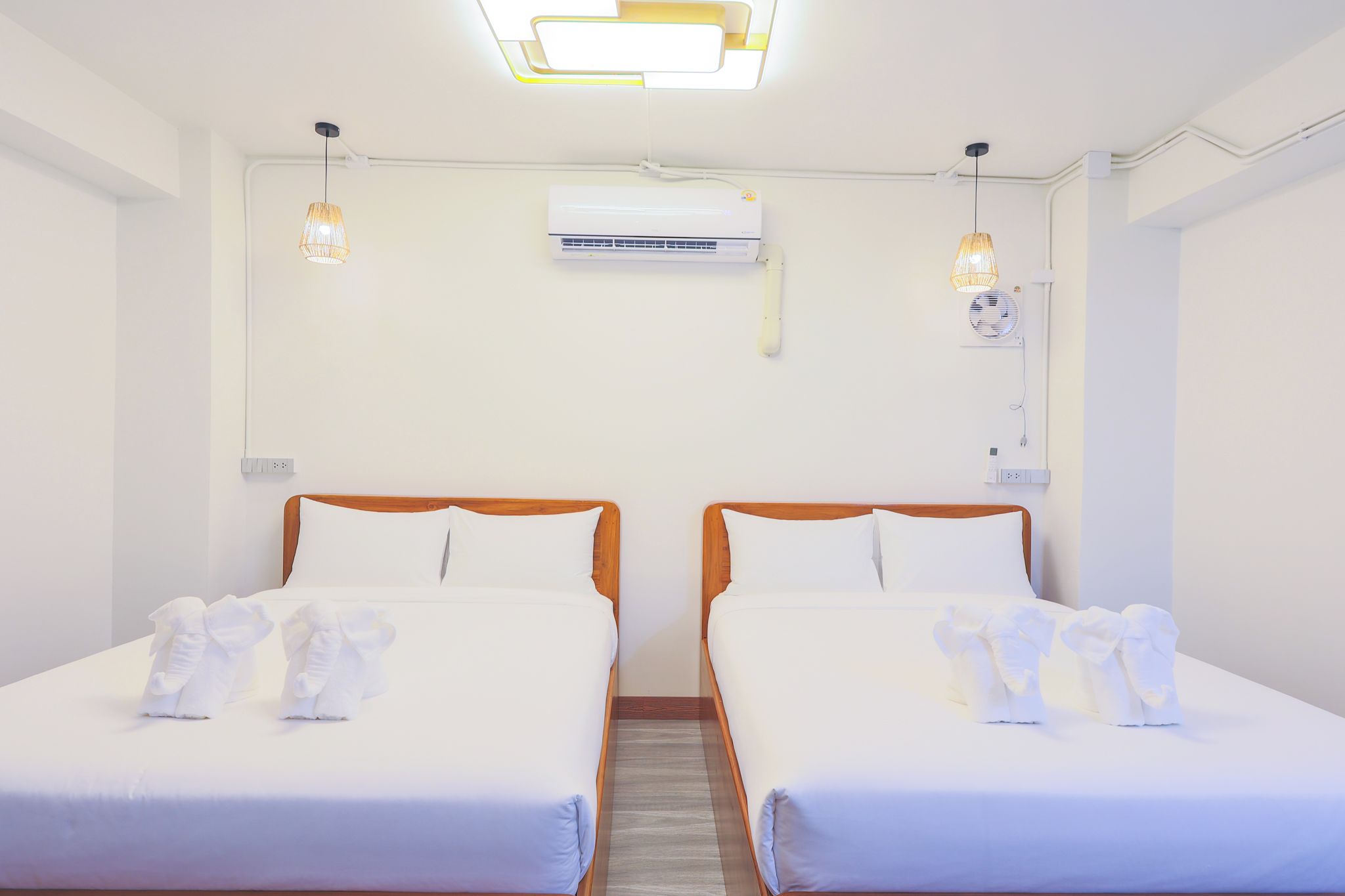 A hotel room with two beds, a ceiling fan, an air conditioning unit, and a wall-mounted light fixture.
