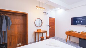 Ein modernes Hotelzimmer mit einem Holzschrank, einem runden Spiegel, einem kleinen Holztisch, einem Bett, einem Fernseher und einer Minibar.