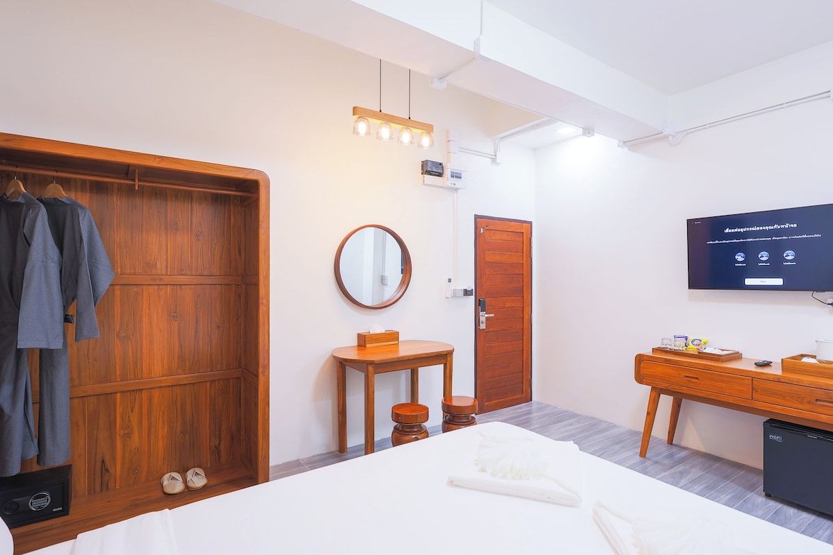 Een moderne hotelkamer met een houten garderobe, een ronde spiegel, een klein houten tafeltje, een bed, een televisie en een minibar.