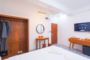 Een moderne hotelkamer met een houten garderobe, een ronde spiegel, een klein houten tafeltje, een bed, een televisie en een minibar.