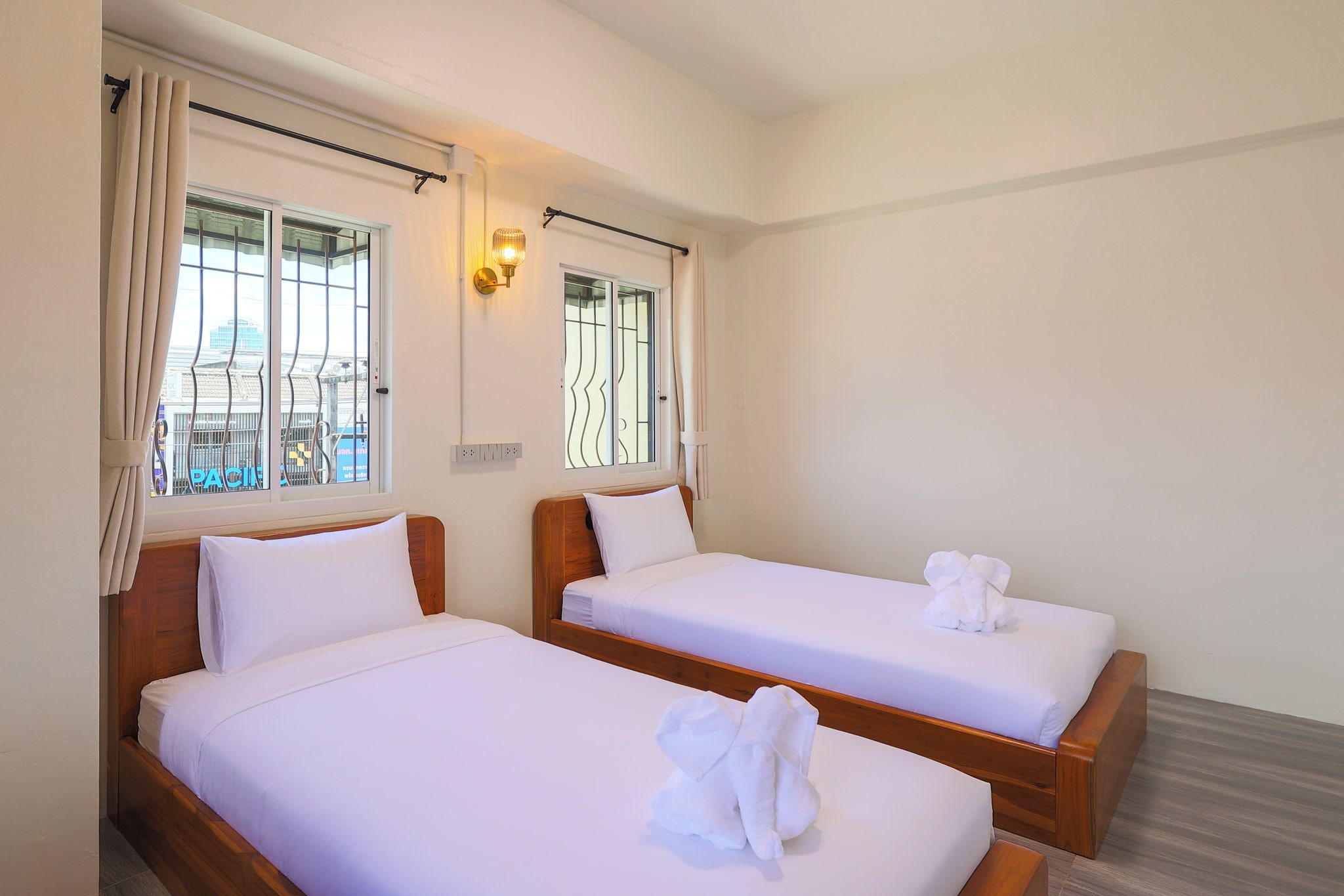 A hotel room with two single beds, a window with curtains, a wall-mounted light fixture, and a view of the cityscape.