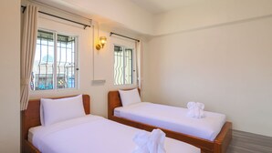 Ein Hotelzimmer mit zwei Einzelbetten, einem Vorhangfenster, einer Wandleuchte und Blick auf die Stadt.