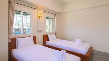 A hotel room with two single beds, a window with curtains, a wall-mounted light fixture, and a view of the cityscape.