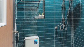 Ein Badezimmer mit Toilette, einer Dusche inklusive Duschbrause und einem Ablagebereich für Pflegeartikel.