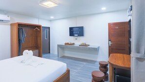 Una habitación de hotel con cama, un armario de madera, un televisor de pantalla plana, una mesita pequeña y una puerta de madera.