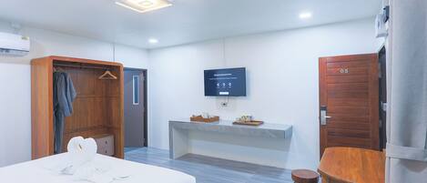 A hotel room with a bed, a wooden wardrobe, a flat-screen TV, a small table, and a wooden door.