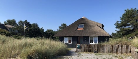 Et hus med stråtækt tag, en træhegn, en grussti og en klar himmel.