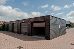 A modern building with a flat roof, large garage doors, and a paved driveway. - Lovely house in Zoutelande for 8 persons - Duinweg 11 (Zoutelande)