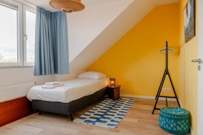 A bedroom with a bed, a bedside table with a lamp, a standing lamp, a patterned rug, and a window with curtains. - Lovely house in Zoutelande for 8 persons - Duinweg 11 (Zoutelande)