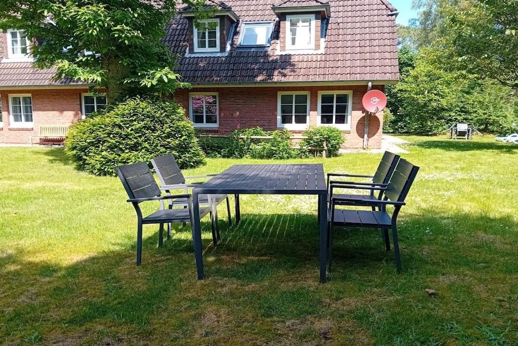 A house with a brick exterior, a tiled roof, and a satellite dish. In the front yard, there is a black metal table with four chairs.