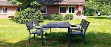 A house with a brick exterior, a tiled roof, and a satellite dish. In the front yard, there is a black metal table with four chairs.