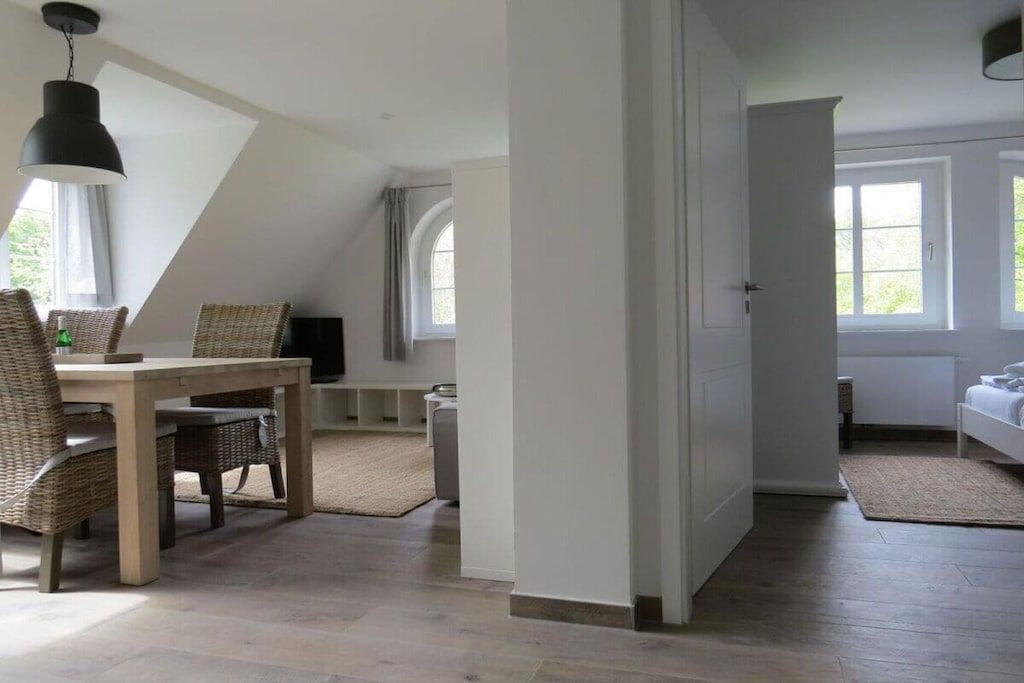A room with a dining table and chairs, a television, and a bed with a window.