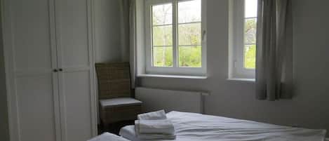 Ein Zimmer mit zwei Betten, einem Fenster mit Vorhängen, einem Heizkörper und einem Kleiderschrank.